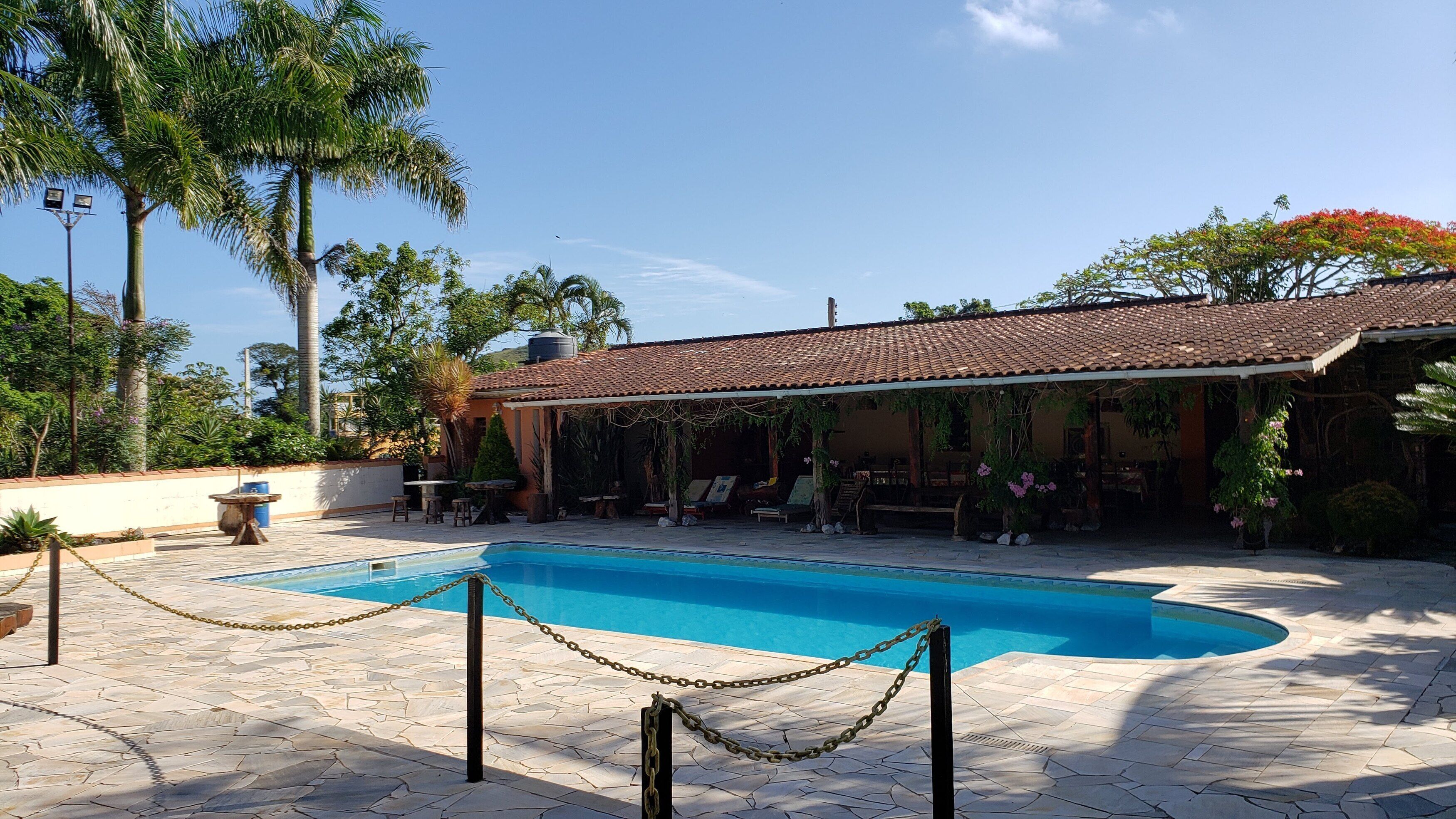 A swimming pool with a tiled deck, surrounded by a covered patio area with outdoor seating.