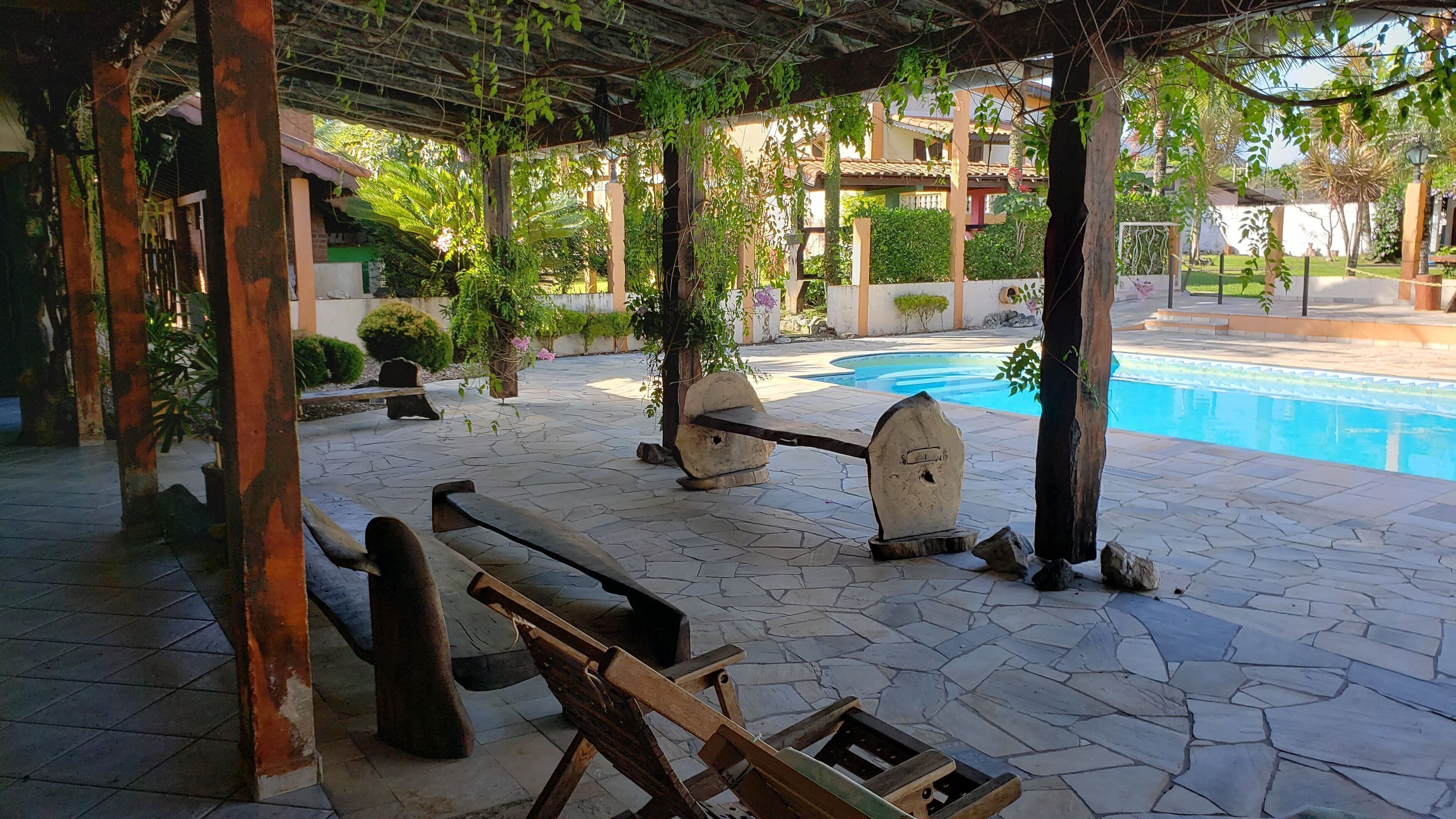 An outdoor pool area with stone flooring, wooden benches, and a pergola structure.