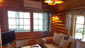 Un interior de cabaña acogedor con un sofá, un televisor sobre un soporte de madera y una mesa.