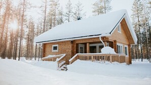 Una cabaña de madera con techo nevado, rodeada de un bosque.