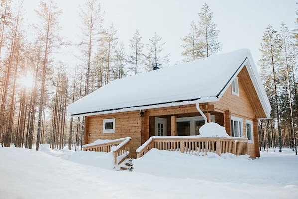 A wooden cabin with a snow-covered roof, surrounded by a forest.