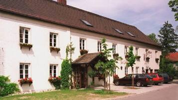 Ein zweigeschossiges Gebäude mit weißer Fassade, zahlreichen Fenstern mit Blumenkästen und einer kleinen Veranda.