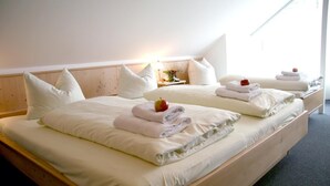 A hotel room with two beds, each with white linens and pillows, and a small table with a lamp and a vase of flowers.