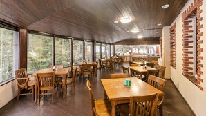 Un comedor amplio con mesas y sillas de madera, ventanas grandes que ofrecen vistas a árboles y una pared de acento de ladrillo.