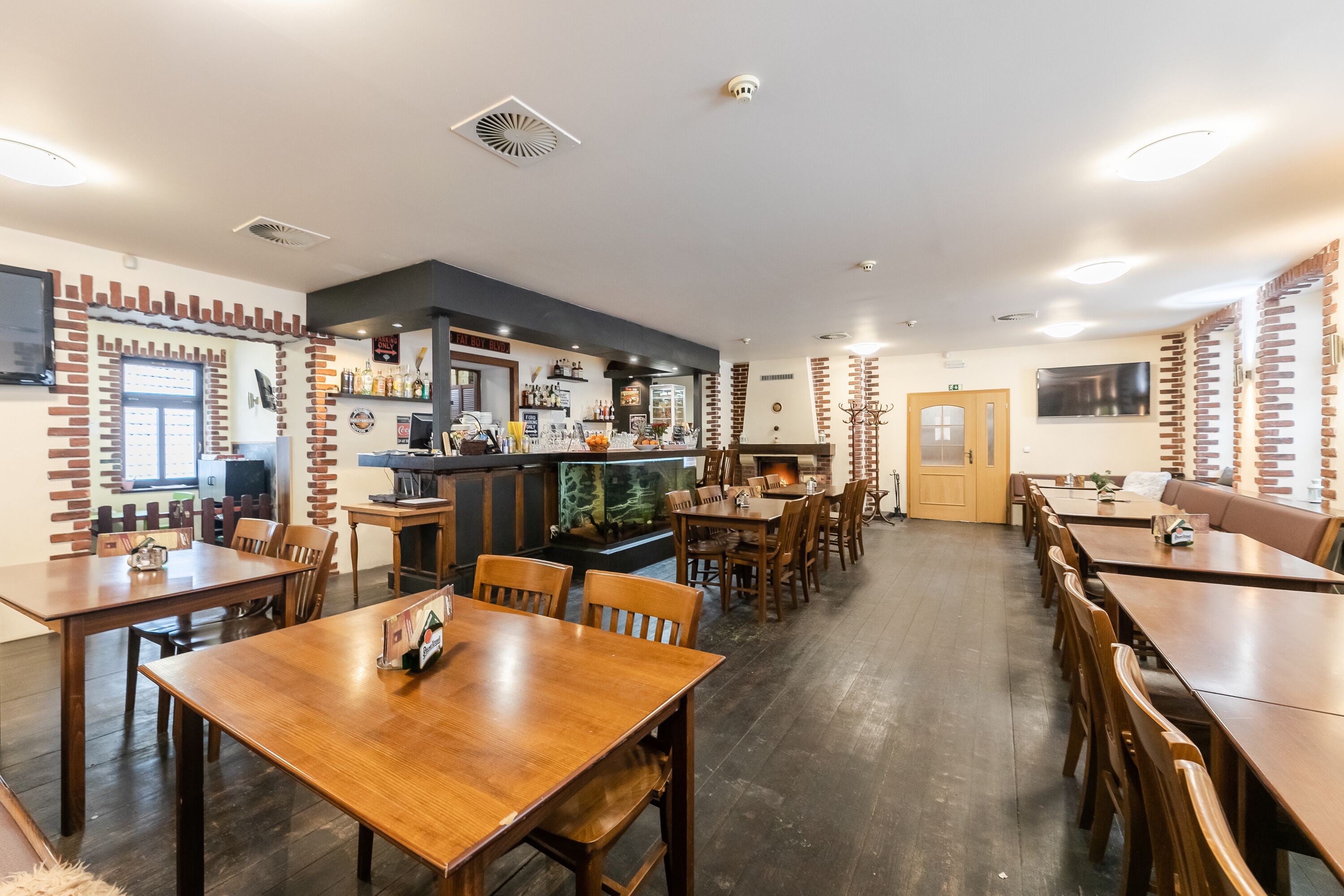A restaurant with wooden tables and chairs, a bar area, and brick accents on the walls.