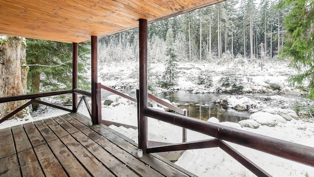 Una terraza de madera con vista a un bosque nevado y un arroyo.