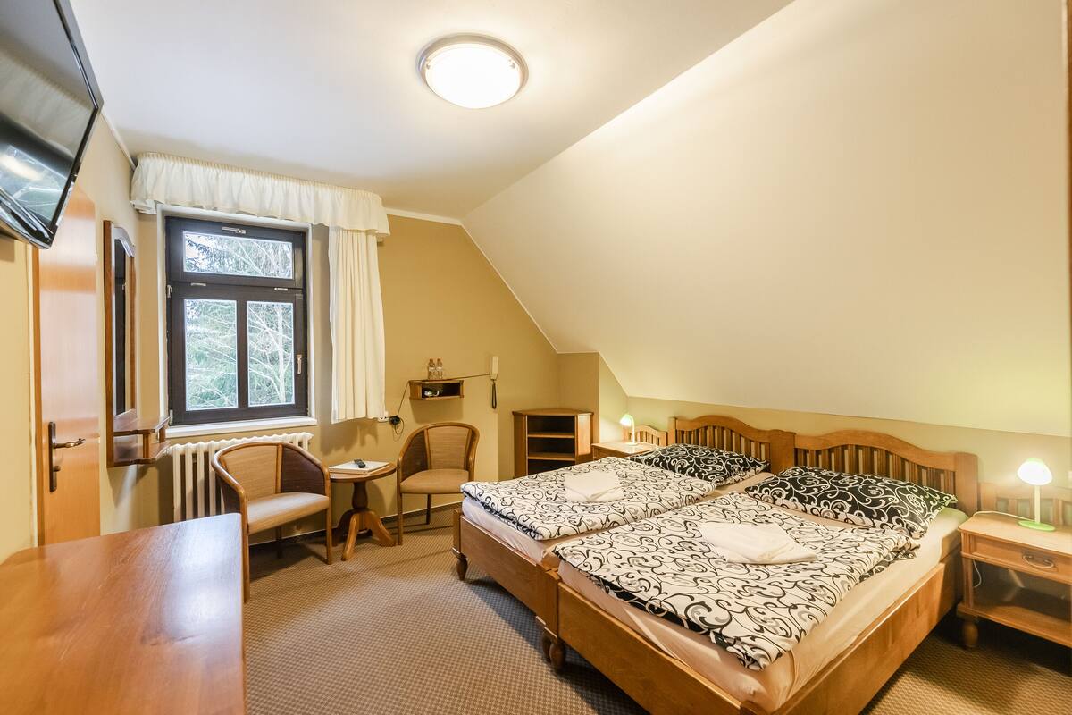 Une chambre avec deux lits, un bureau, une chaise, une télévision et une fenêtre avec des rideaux.