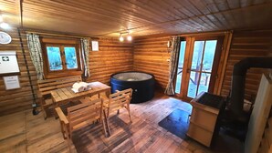 Interior acogedor de una cabaña con paredes de madera, una mesa de madera con sillas, un jacuzzi y una chimenea.