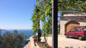 A red car parked on a road with a stone bridge and a view of the sea. - Villa Stefano lake view (Gargnano)