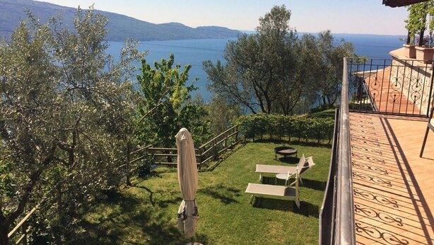 A terrace with a view of a lake, a grassy area with a table and chairs, and a pergola with an umbrella. - Villa Stefano lake view (Gargnano)