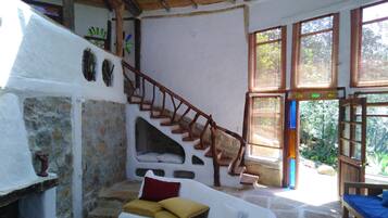 A rustic interior with a stone wall, a wooden staircase, a white sofa, and a bed.