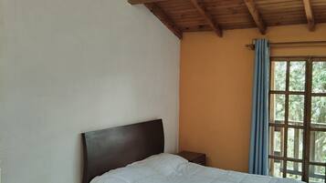 A bedroom with a wooden ceiling, a bed with a white duvet, a nightstand, and a window with a blue curtain.