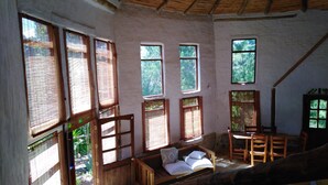 Una habitación rústica con techo de paja, muebles de madera y amplias ventanas que dejan entrar la luz natural.