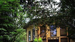 Un edificio rústico con amplias ventanas y un jardín con diversas plantas y un banco de madera.