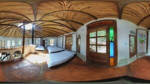 Una habitación con techo curvo, una cama, un ventanal con tonalidad verdosa y una puerta de madera.