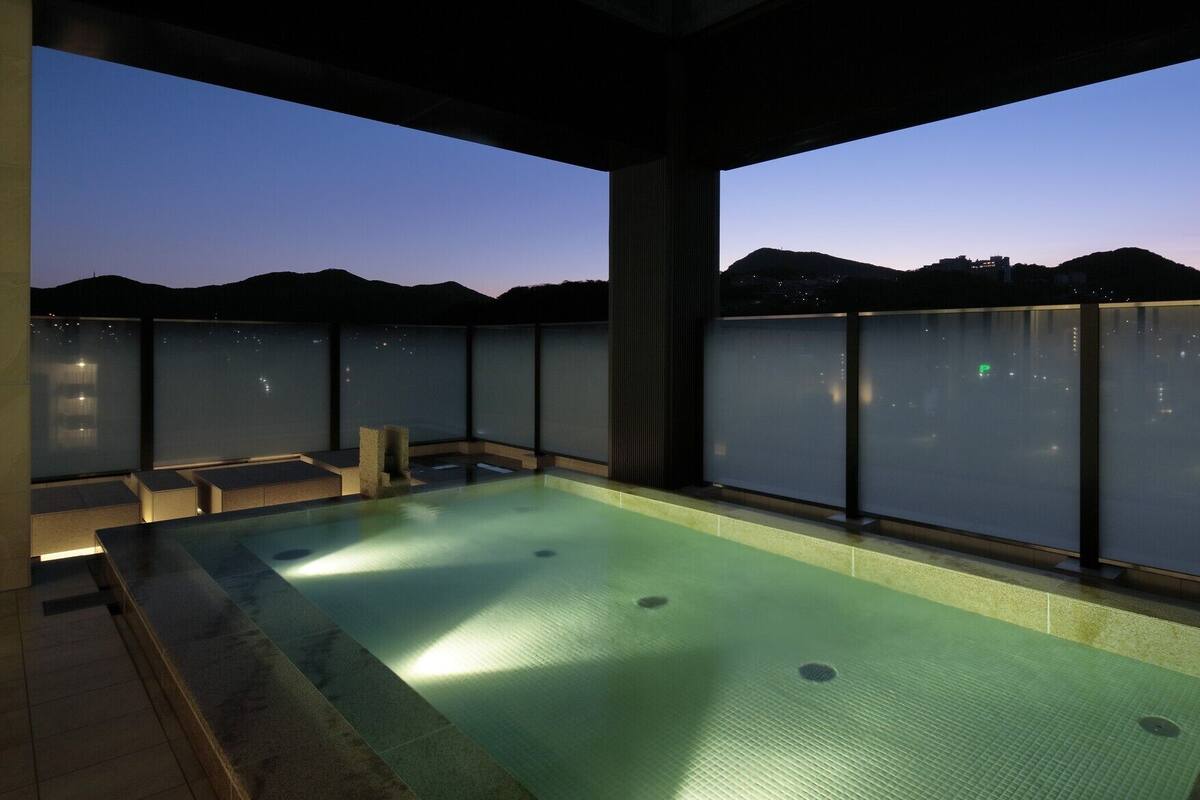 Una piscina infinita en la azotea con vistas despejadas al horizonte urbano al atardecer.