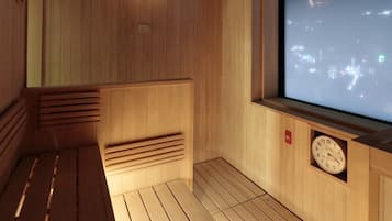 A sauna room with wooden walls, a bench, a clock, and a large window with a cityscape view.