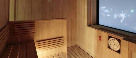 A sauna room with wooden walls, a bench, a clock, and a large window with a cityscape view.