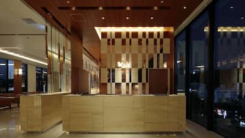 A modern hotel reception area with a wooden reception desk, a star logo, and a large window offering a city view.