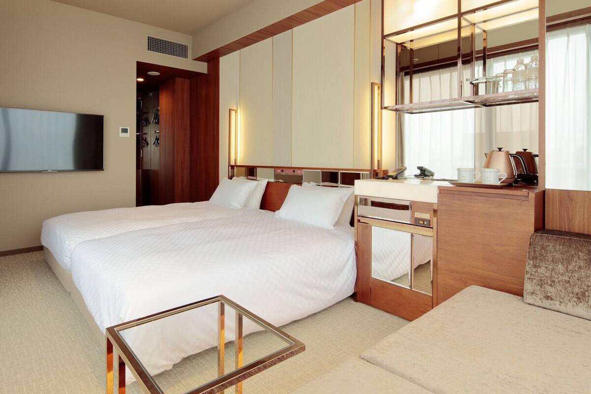 A hotel room with a bed, a TV, a desk with a mirror, and a coffee maker.