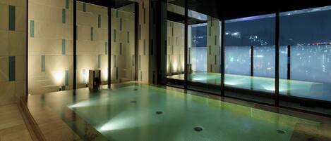 An indoor swimming pool with a city view, tiled walls, and a wooden ceiling.