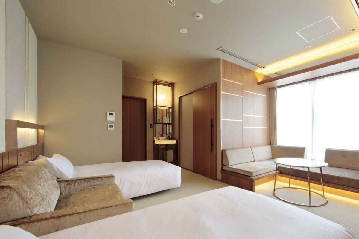 Una habitación de hotel con dos camas, un sofá, una mesita y un ventanal grande.