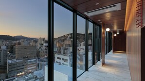 Un pasillo moderno de hotel con amplios ventanales que ofrecen vistas a la ciudad, techo de madera y un letrero que dice "SKY SPA MOME".