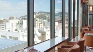 Una habitación de hotel moderna con ventanas amplias, un balcón con asientos y vistas a la ciudad.