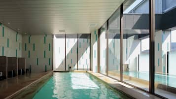 An indoor swimming pool with clear glass walls, a tiled floor, and a ceiling with recessed lighting.