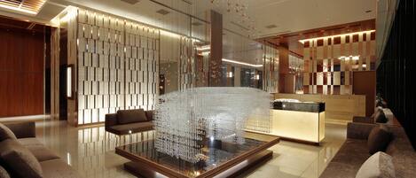 A modern lobby with a central glass table, seating areas, and a reception desk.