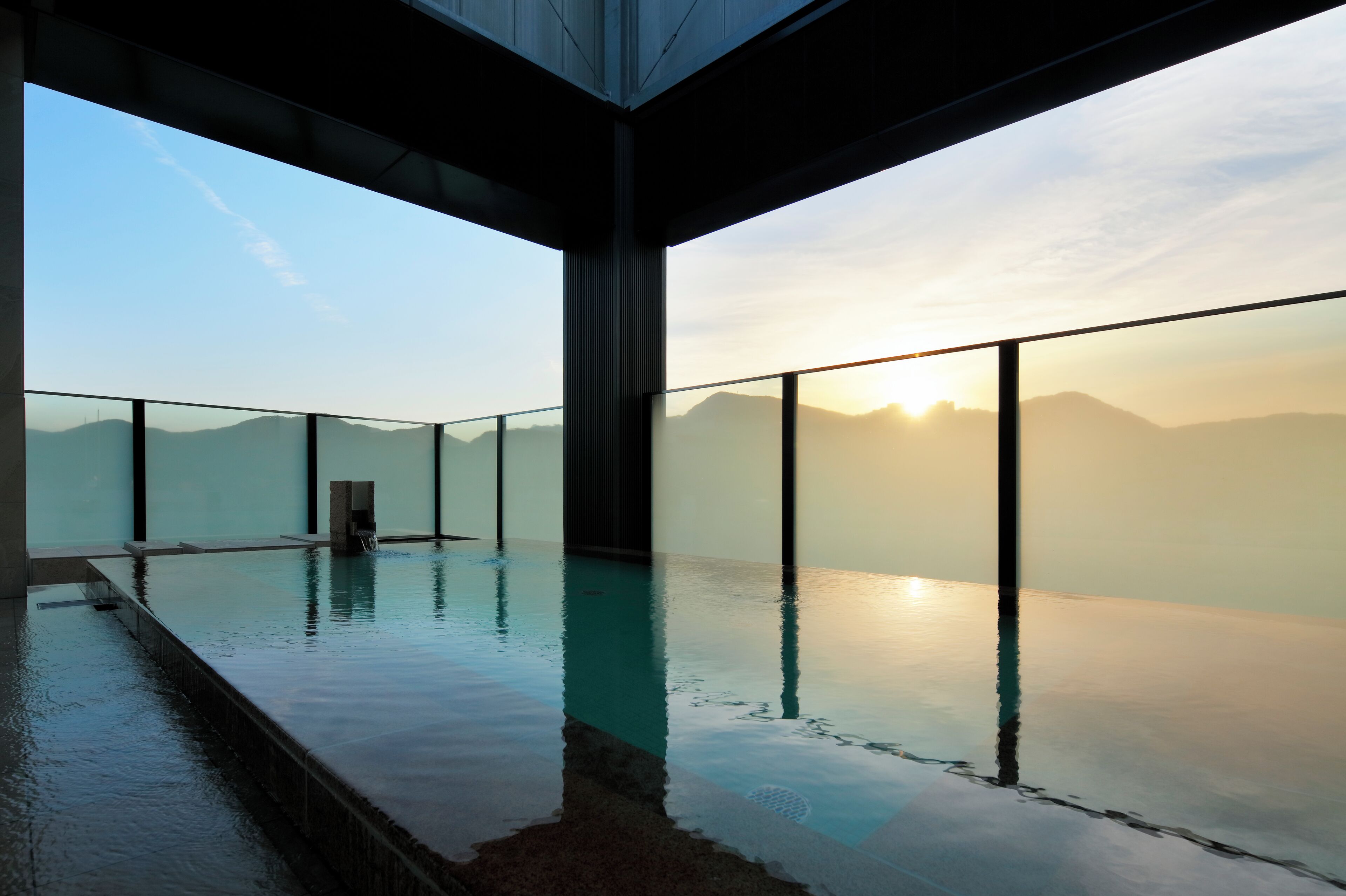 Una piscina infinita con vistas a montañas y al sol poniéndose.