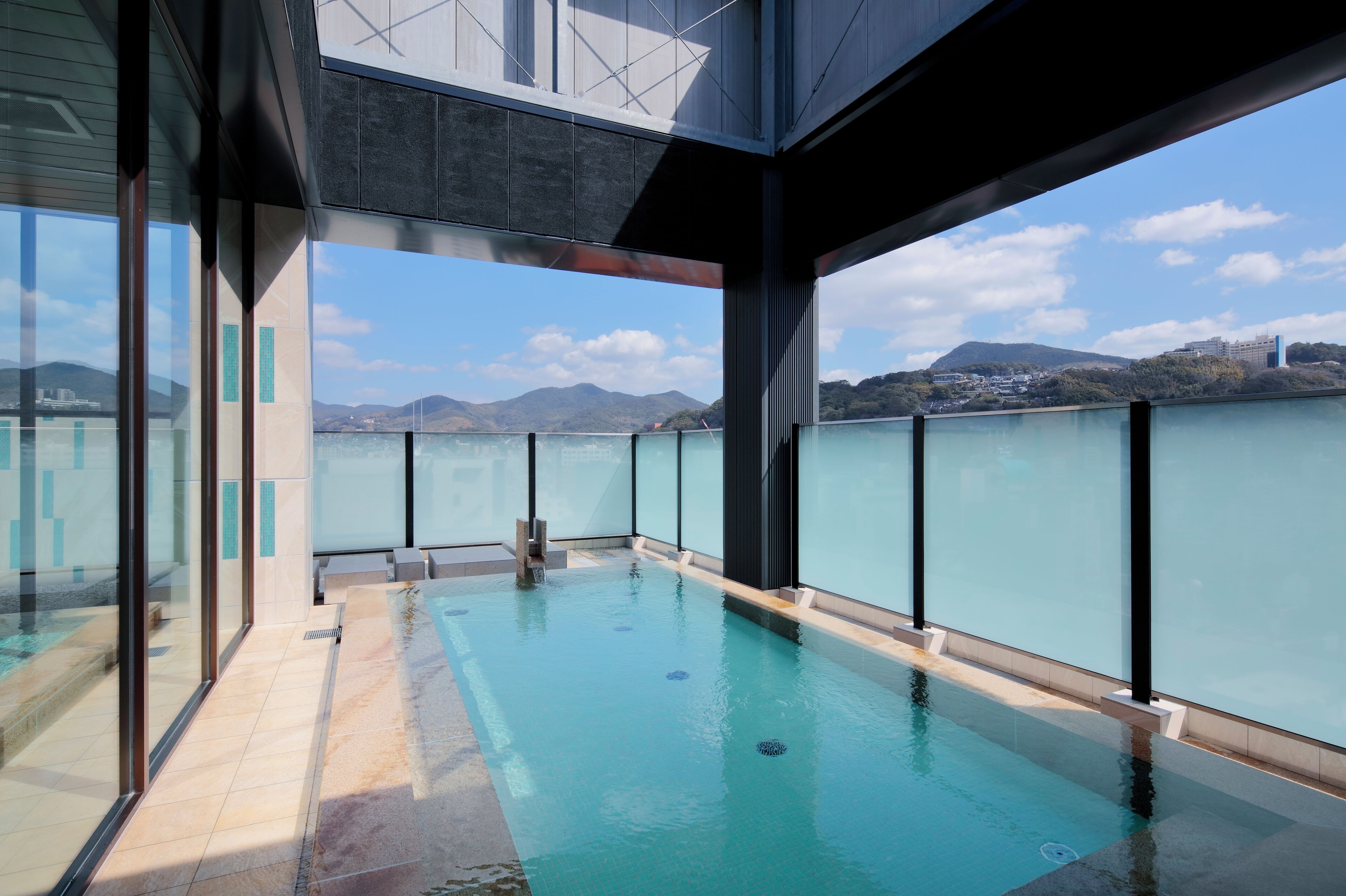 Une piscine intérieure moderne avec des murs en verre, offrant une vue dégagée sur un paysage montagneux, et un espace aménagé au bord de la piscine.
