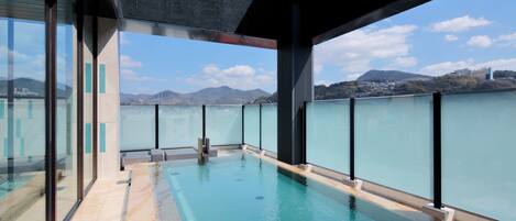 A modern indoor pool with glass walls, a clear view of a mountainous landscape, and a poolside area.