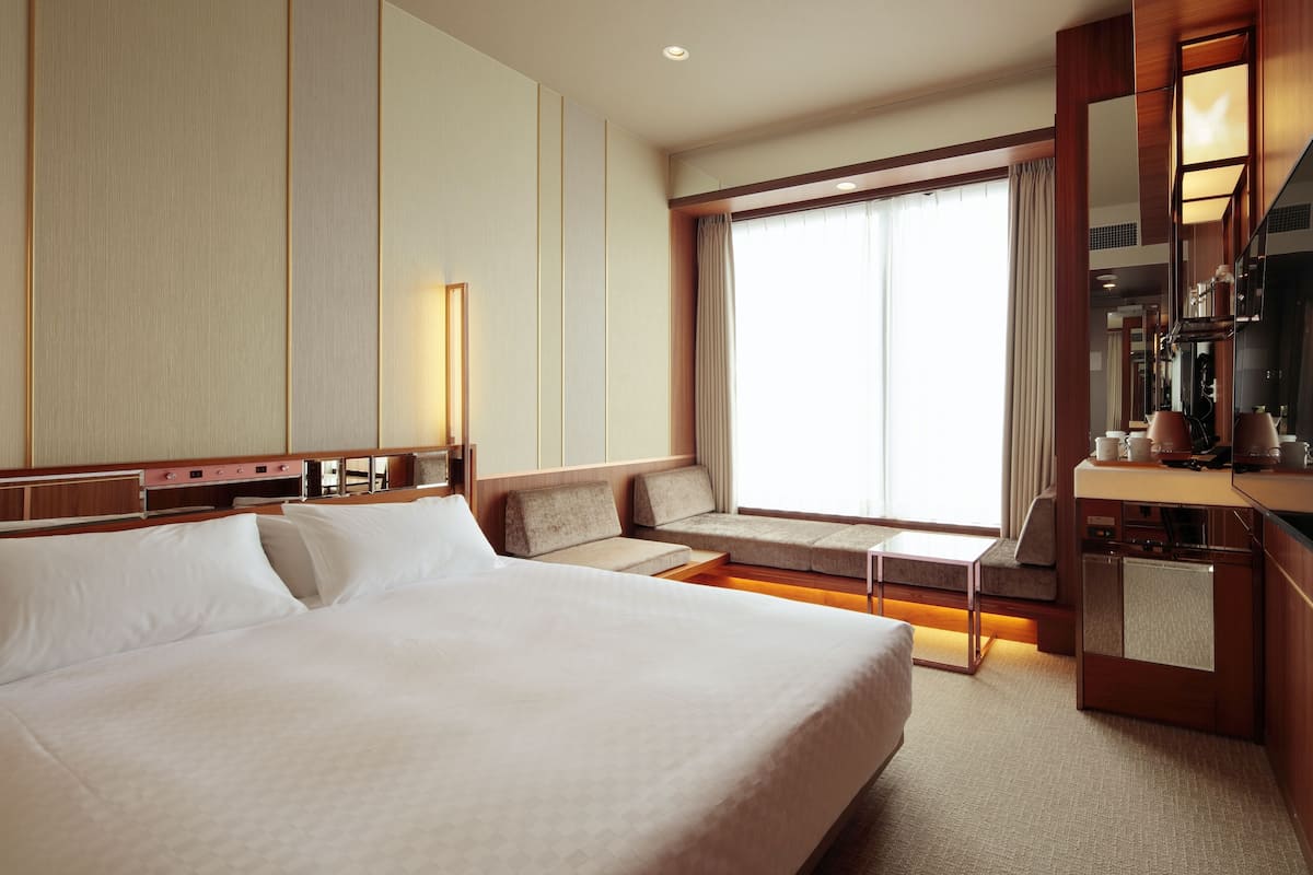 Habitación de hotel con una cama grande, zona de estar con vistas a la ciudad y un minibar.