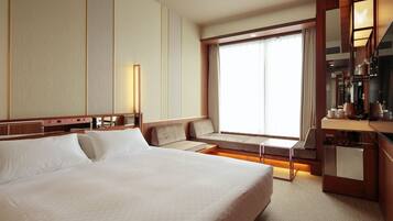 Habitación de hotel con una cama grande, zona de estar con vistas a la ciudad y un minibar.