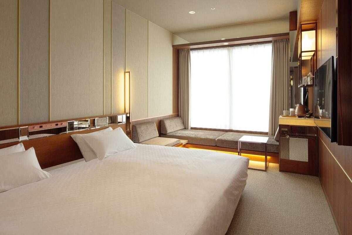 Una habitación de hotel con una cama grande, una zona de estar con cojines, un televisor y un minibar.