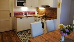 Una cocina compacta con armarios blancos, un microondas, una estufa y un lavamanos. El piso tiene un diseño y hay una mesa con sillas.