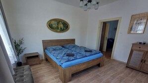 Un dormitorio con cama de madera, un banco, una planta en maceta y una puerta que da a otra habitación.