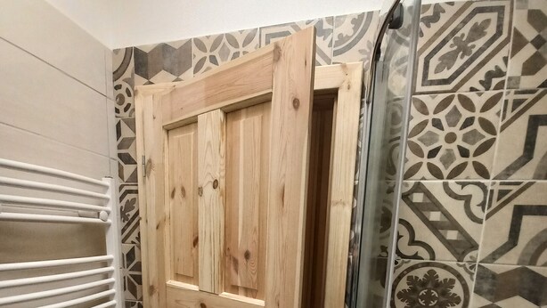 Un baño con puerta de madera, zona de ducha y baldosas estampadas.