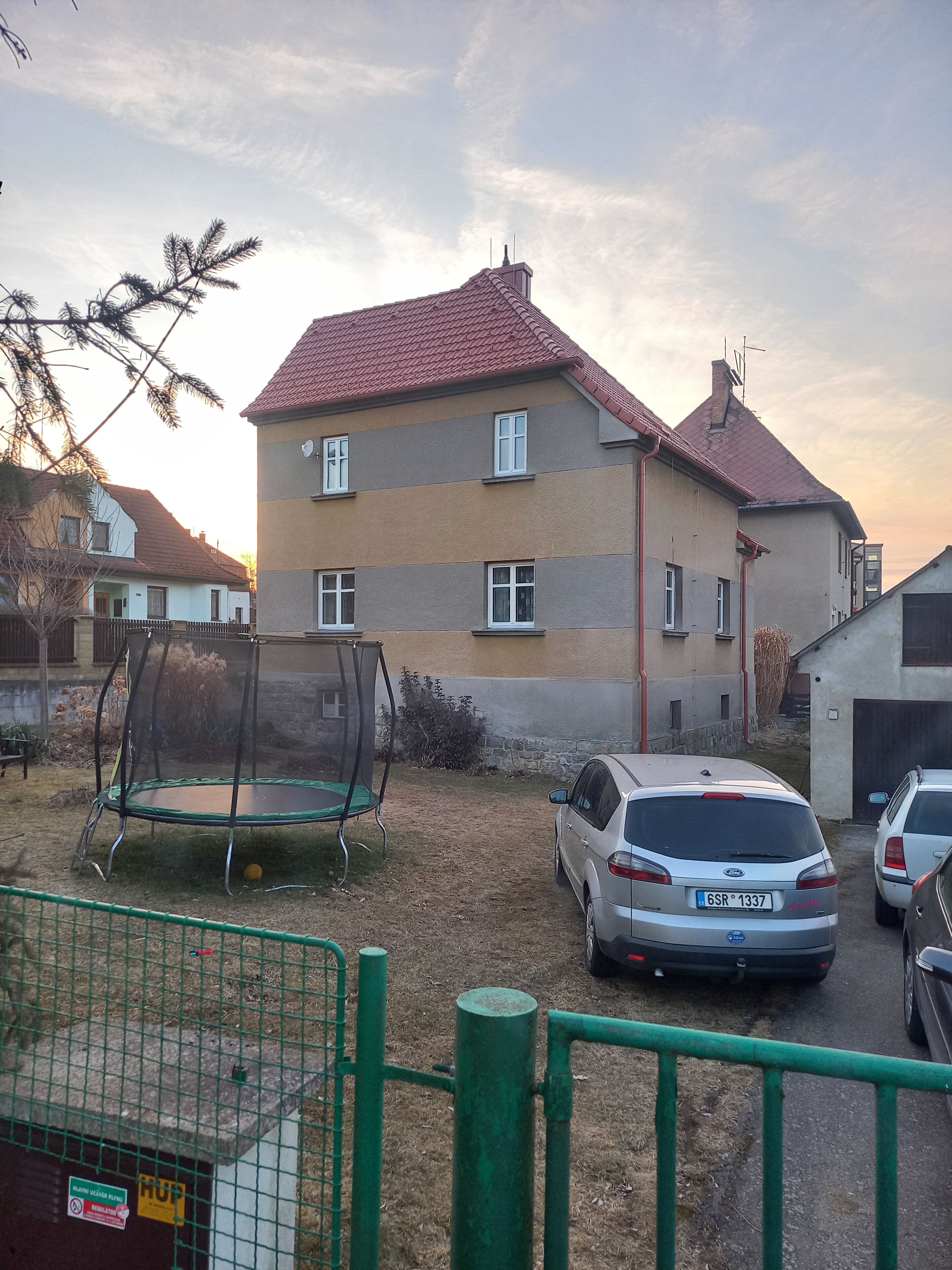 Um bairro residencial com uma casa de dois andares, um trampolim e carros estacionados.