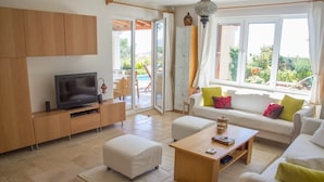A modern living room with a TV, sofa, ottoman, and coffee table. - Villa Bethany (Kalkan)