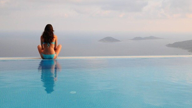 Una persona sentada al borde de una piscina con vista al mar y a islas distantes.