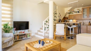 Una sala de estar moderna con un televisor, una mesa de centro y una escalera que lleva a una cocina.