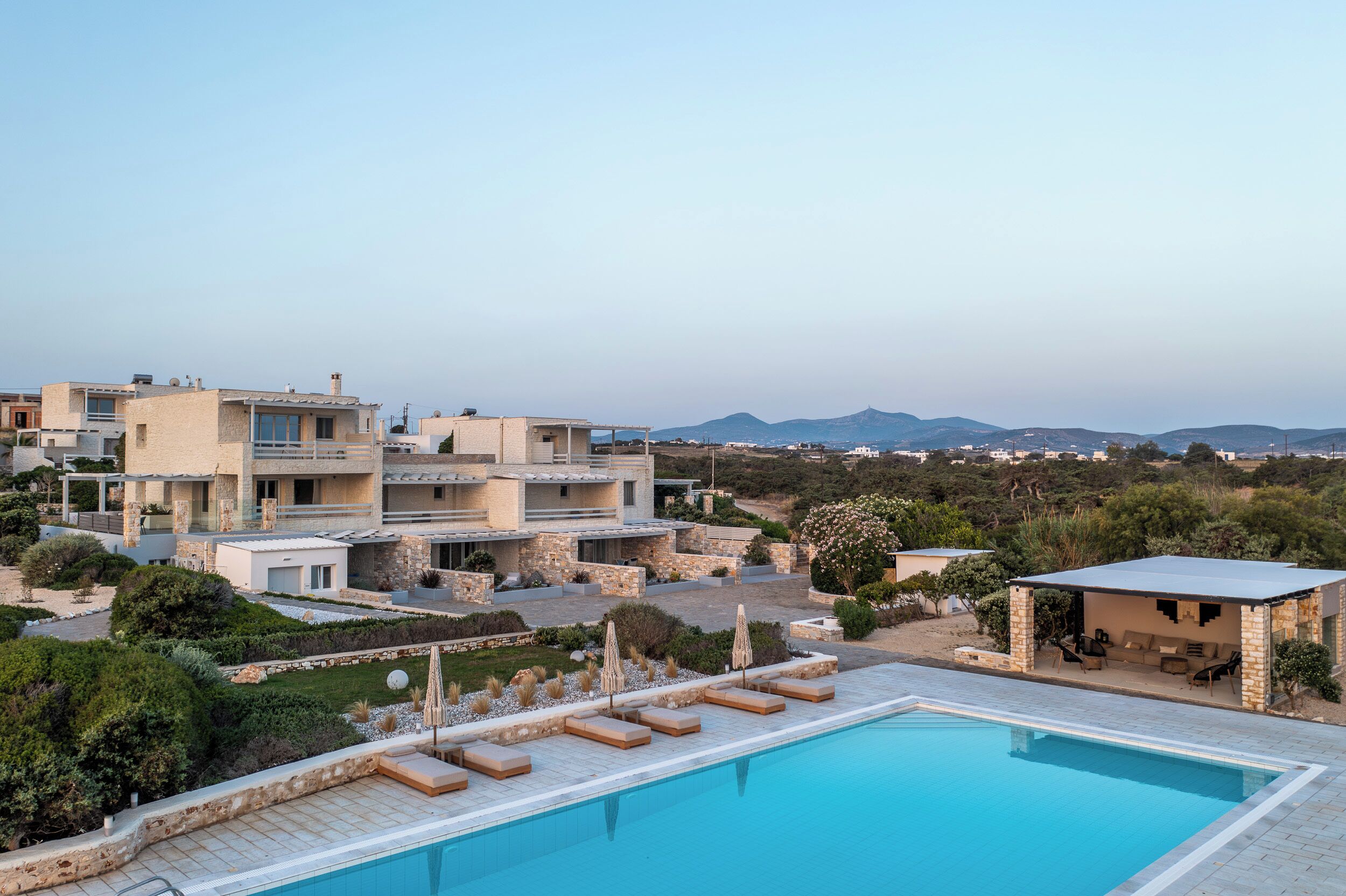 A modern villa with a swimming pool, outdoor seating, and a view of the surrounding landscape.