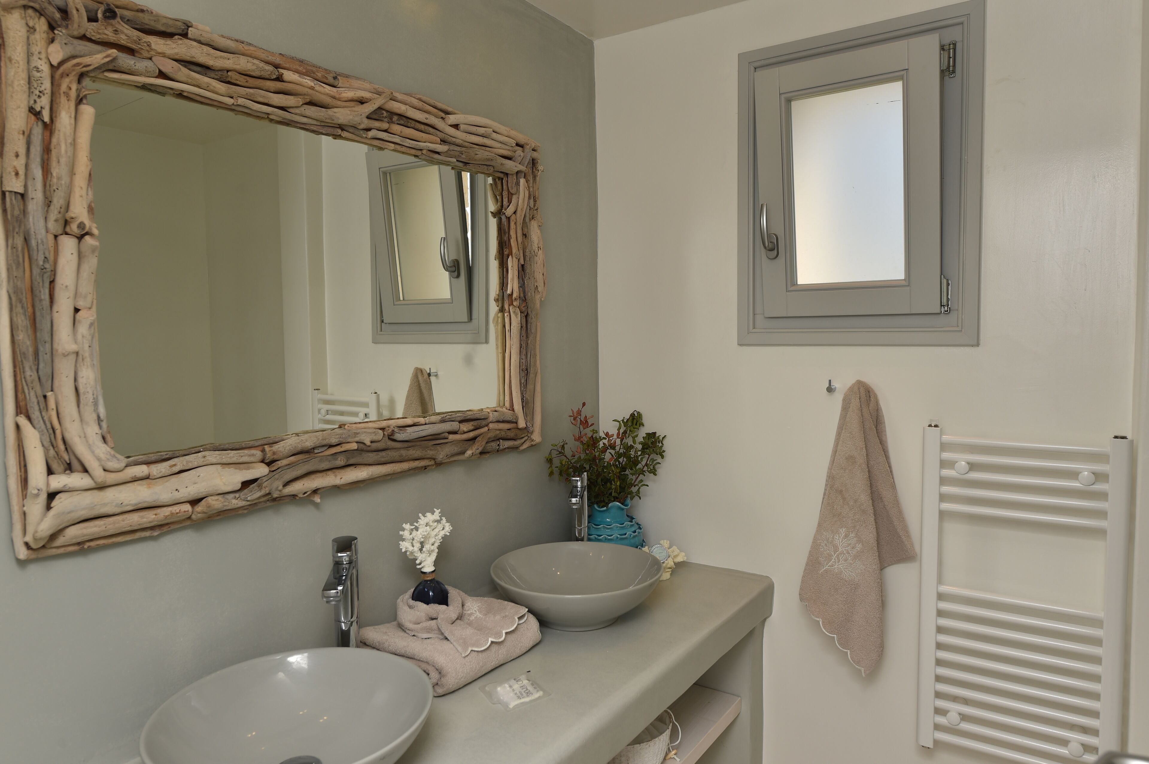 A bathroom with a rustic mirror, a large sink, a towel rack, and a radiator.