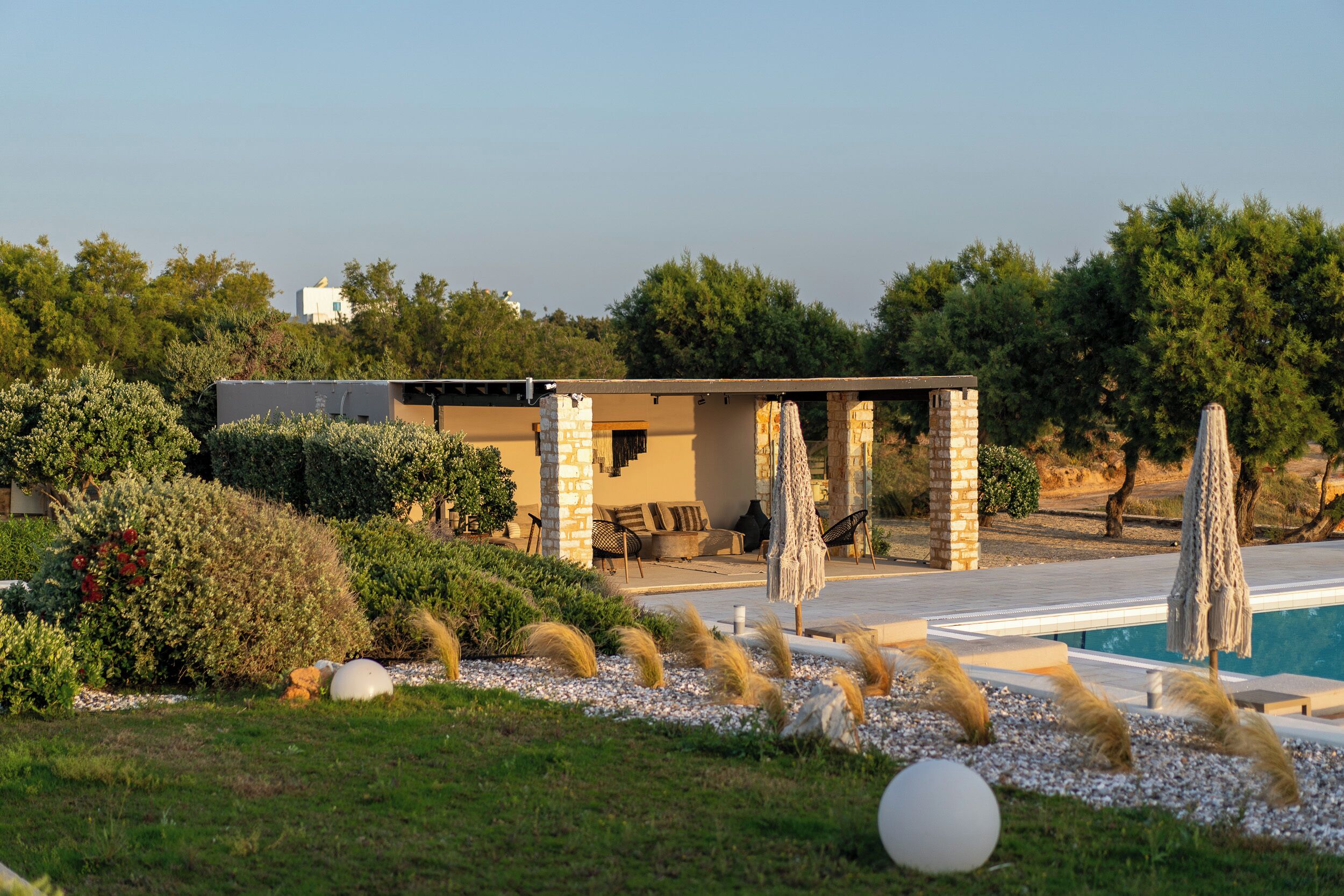A modern outdoor pool area with a stone structure, lounge chairs, and umbrellas.