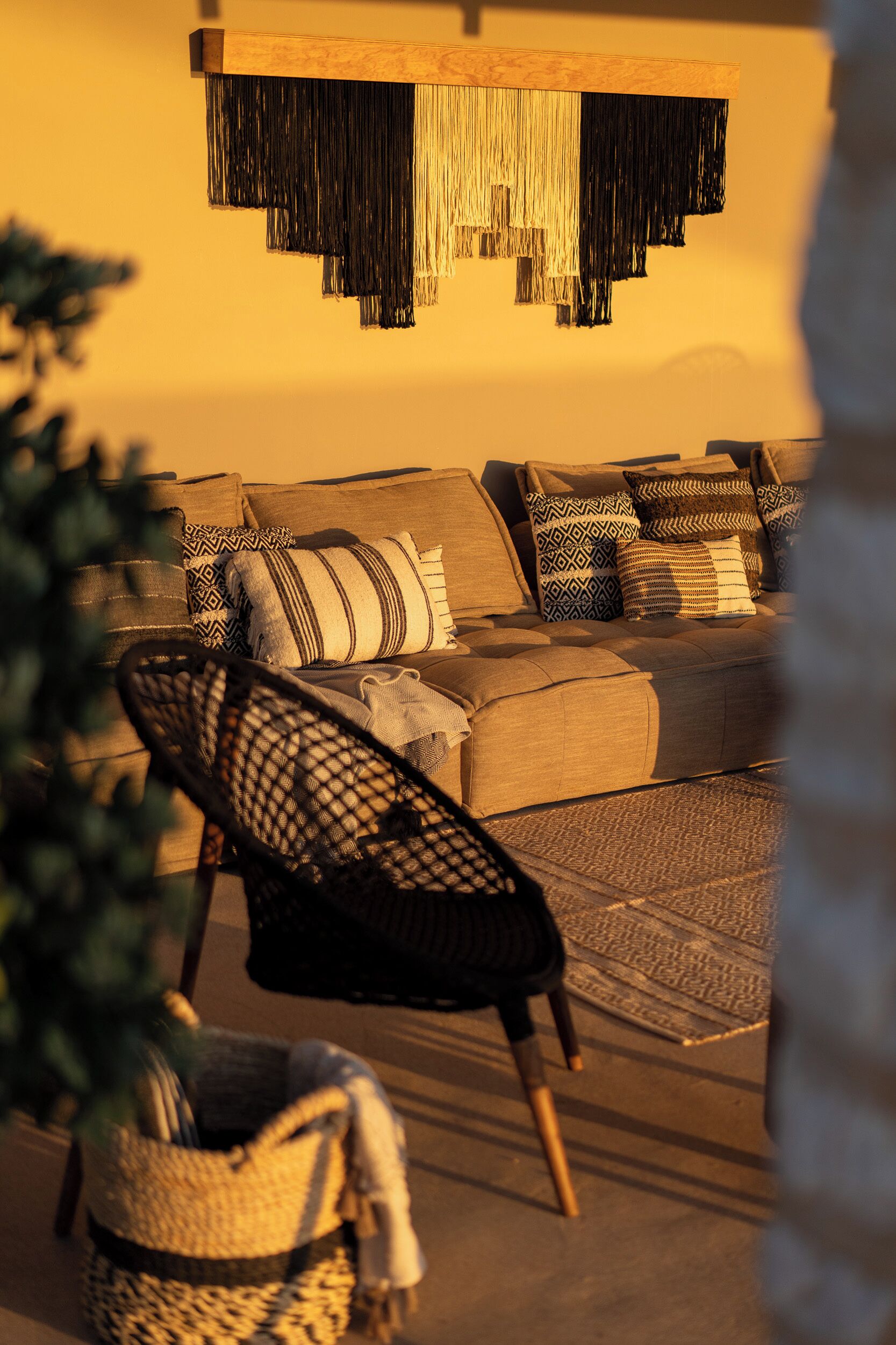 A living room with a sofa, patterned cushions, a woven chair, and a hanging light fixture.