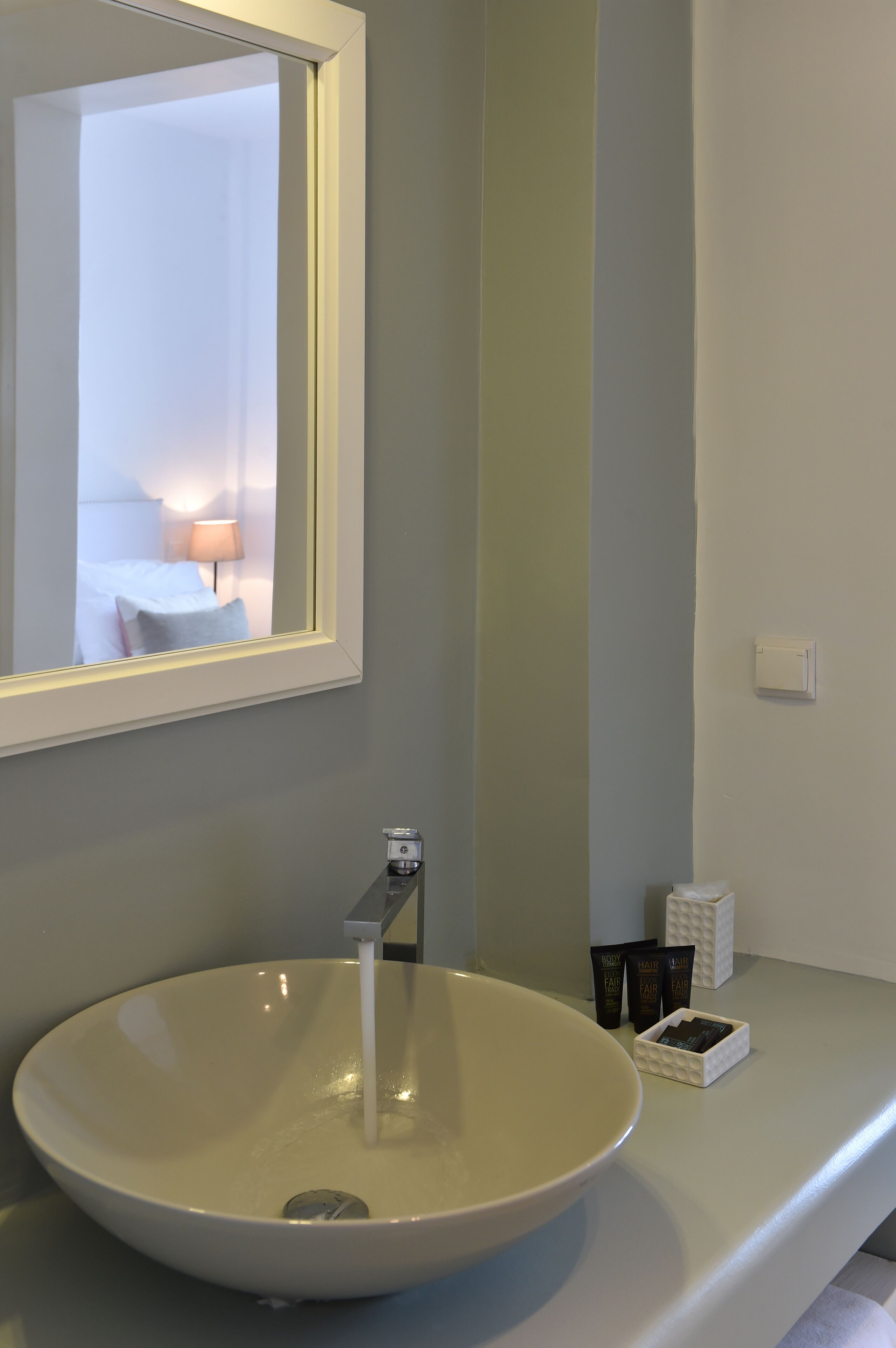 Un baño con lavamanos blanco, un espejo y artículos de aseo en la encimera.