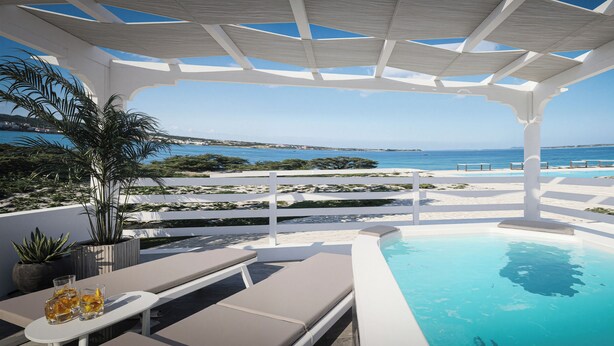 Uma área de piscina com vista para o mar, uma pérgula, cadeiras de descanso e plantas em vasos.