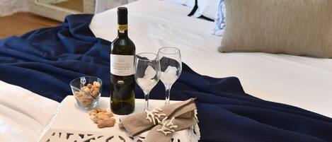 A neatly arranged bed with a bottle of wine, two glasses, and a bowl of nuts on a white tray.